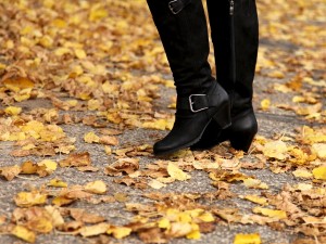 Frauenbeine in kniehohen Stiefeln und gelbe Blätter im Herbst