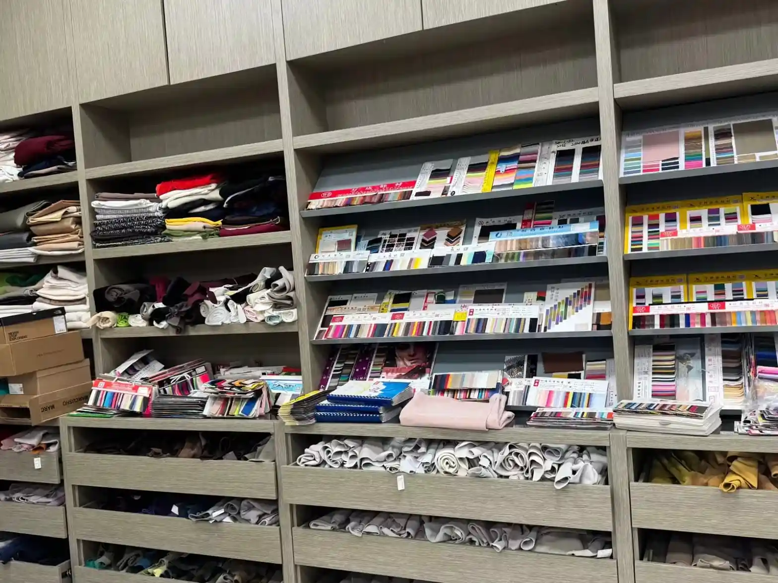 A full wall of material library shelving with rolled leathers, swatch stacks, colour card binders and in-stock swatch boxes